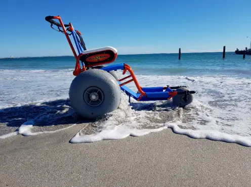 Beach wheelchair with large balloon tires at the shoreline as waves wash over the sand